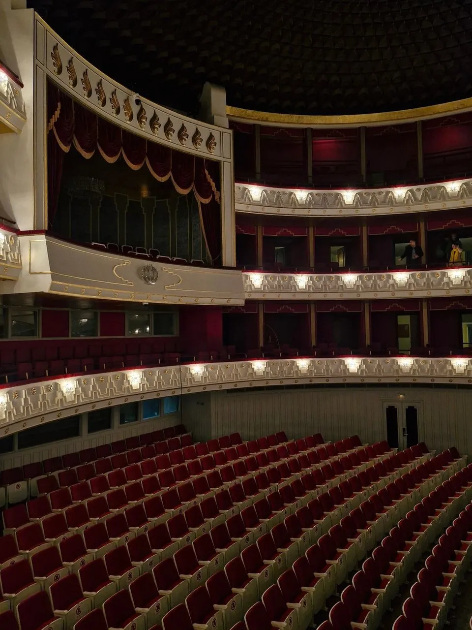 Interiorul unui auditorium cu rânduri de scaune roșii și balconuri decorate cu elemente albe și draperii roșii.