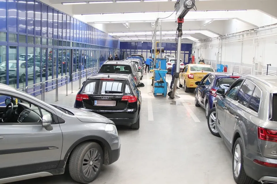 Mai multe mașini sunt parcate într-un atelier de service auto cu podea albă și panouri de sticlă albastră pe lateral.