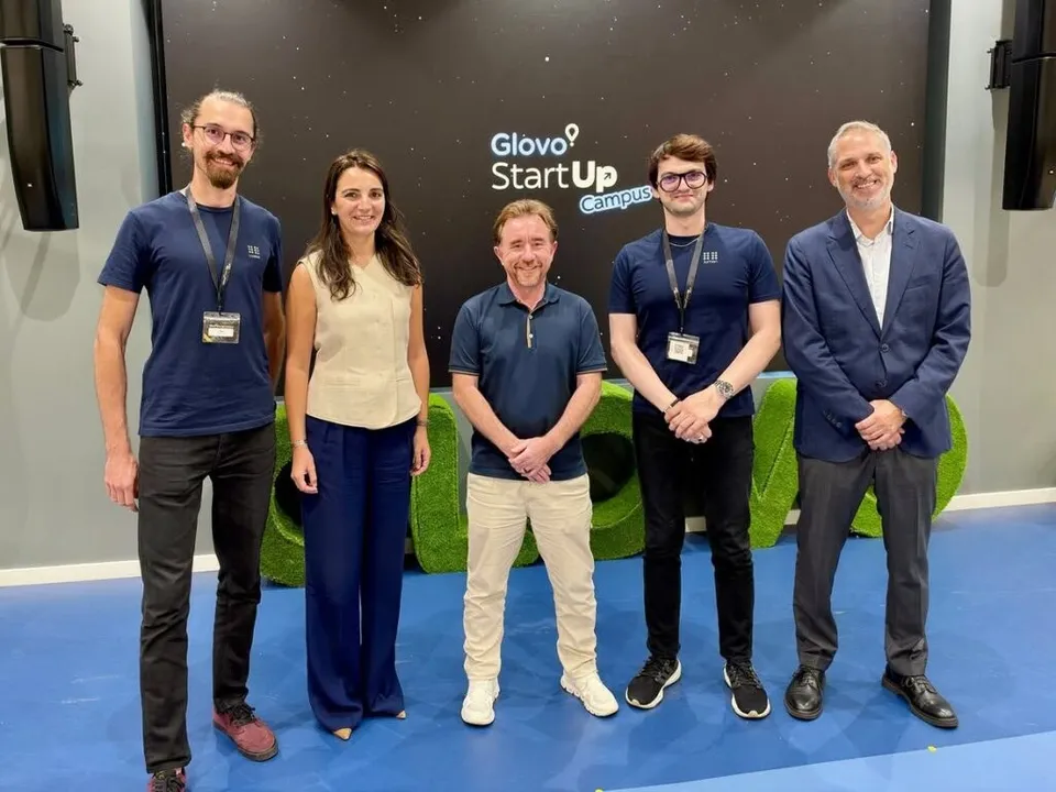Cinci persoane stau în picioare în fața unui panou negru pe care scrie Glovo StartUp Campus.
