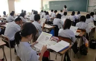 Elevi în uniforme albe stau la bănci într-o sală de clasă și lucrează cu manuale și caiete deschise.