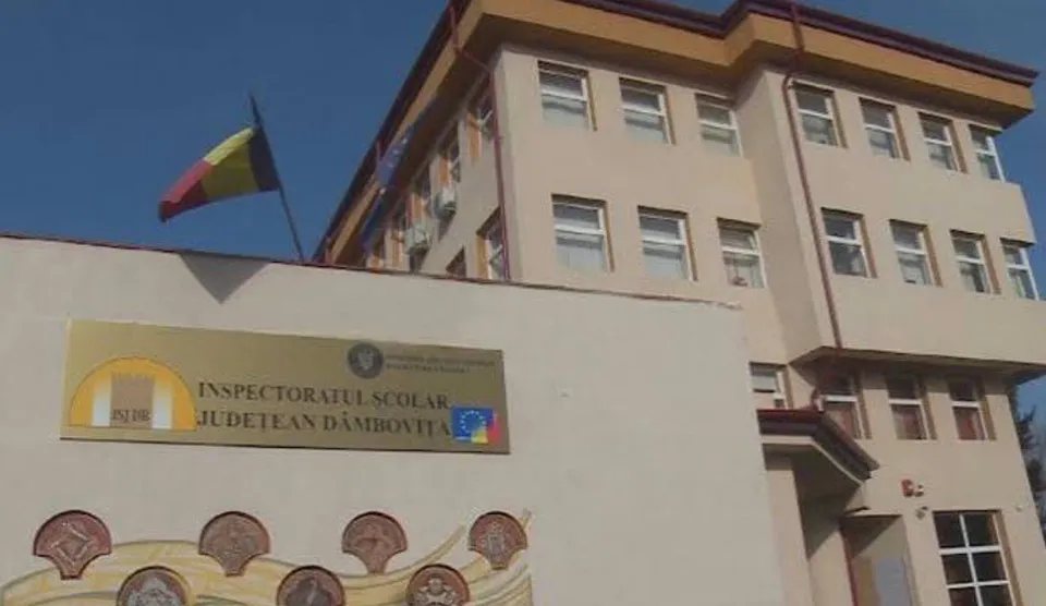 O clădire cu ferestre dreptunghiulare și un steag tricolor agățat pe un stâlp sub un cer senin.