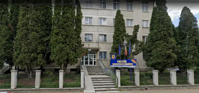 O clădire cu ferestre multiple este încadrată de copaci înalți și are o scară de acces în fața unei intrări cu uși de sticlă.