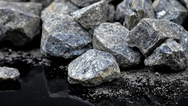 Grup de pietre gri și gri-albastre cu suprafețe neregulate, așezate pe o suprafață neagră și lucioasă.