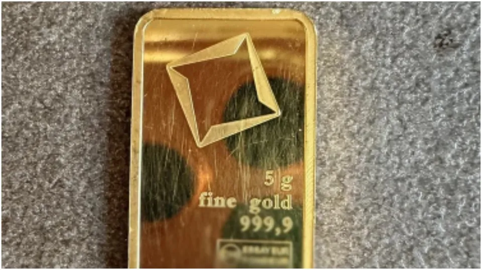 Un obiect dreptunghiular de culoare aurie prezintă inscripția fine gold 999,9 și cifra 5 g pe o suprafață lucioasă.