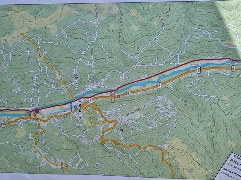 O hartă topografică detaliată prezintă linii de contur, drumuri colorate și zone verzi pe un fundal de relief montan.