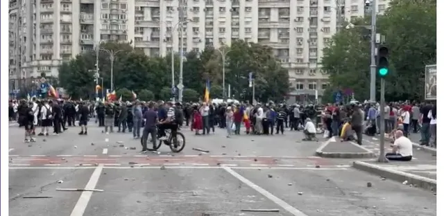 O mulțime de oameni stă pe o stradă largă în fața unor clădiri înalte, având obiecte împrăștiate pe asfaltul din prim-plan.