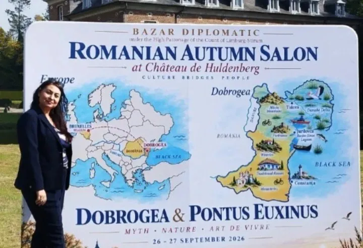O femeie cu părul negru și o jachetă închisă la culoare stă lângă un panou informativ alb cu hărți și text colorat.