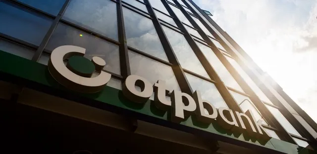 Un semn cu textul „otpbank” este montat pe fațada unei clădiri cu ferestre mari de sticlă sub un cer luminos.