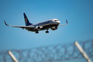 Un avion de pasageri cu marcajul Ryanair zboară pe un cer albastru cu trenul de aterizare extins.