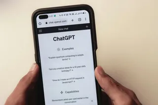 O pereche de mâni ține un smartphone afișând interfața aplicației ChatGPT, cu un meniu de exempluri și capacități pe ecran.