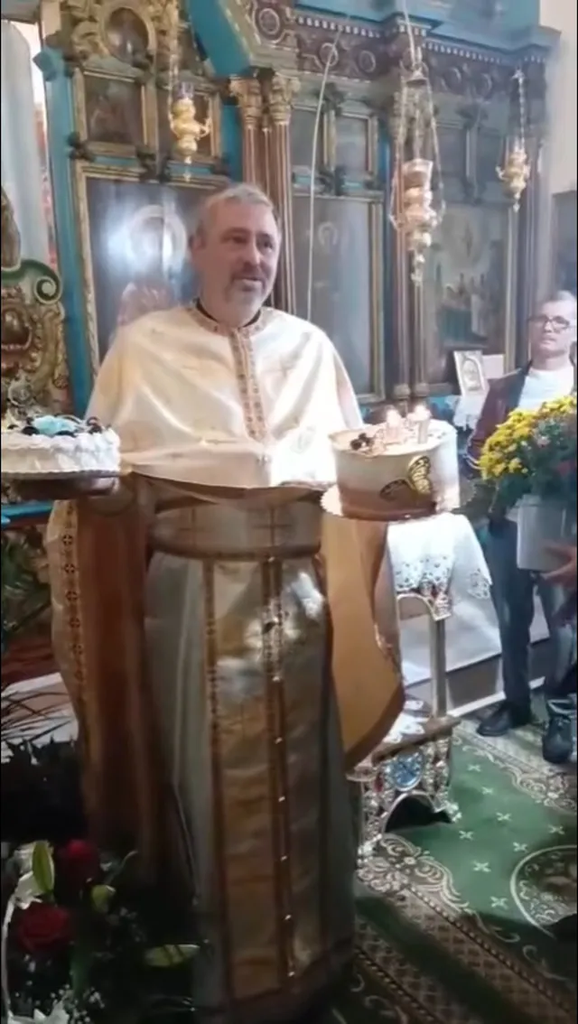 Un bărbat cu barbă poartă haine liturgice de culoare deschisă în fața unui iconostas decorat cu coloane și picturi religioase.
