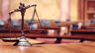 O balanță metalică cu două taleri este așezată pe o suprafață de lemn într-o încăpere cu mobilier de lemn în fundal.