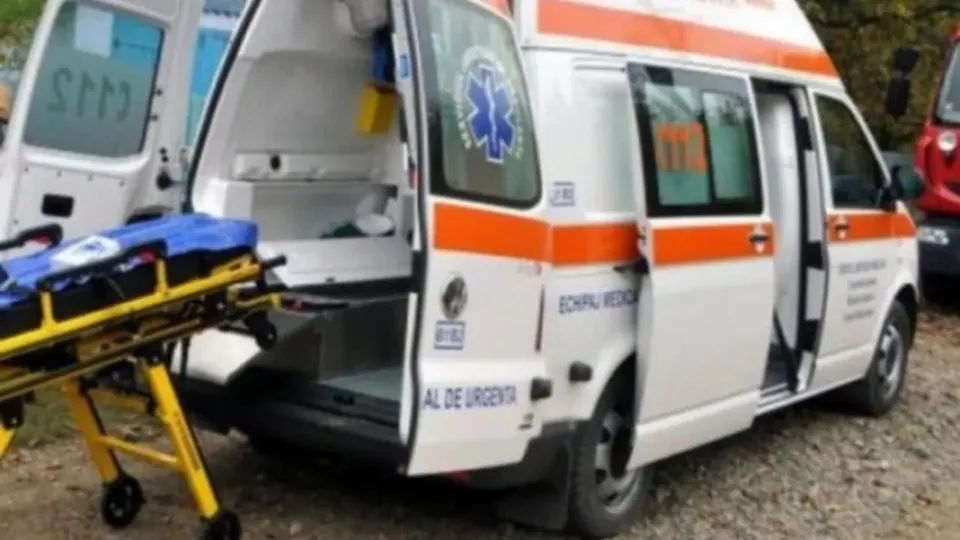 O ambulanță albă cu dungi portocalii este parcată cu portierele deschise, afișând un pat de transport medical pe exteriorul vehiculului.
