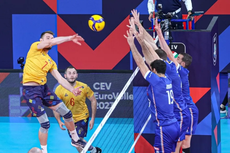 Jucători de volei, unii în galben și alții în albastru, sar lângă fileu după o minge, pe un fond geometric.
