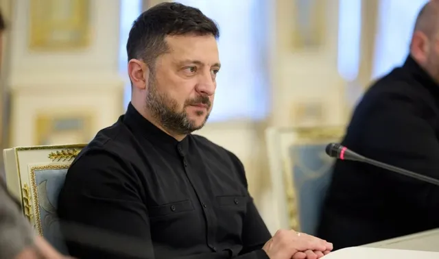 Un bărbat cu barbă și păr scurt, îmbrăcat în tricou negru, stă la o masă lângă un microfon.