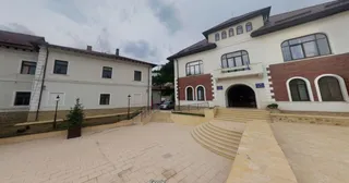 O clădire cu fațadă albă și secțiuni din cărămidă roșie prezintă ferestre negre și o intrare cu trepte curbe.