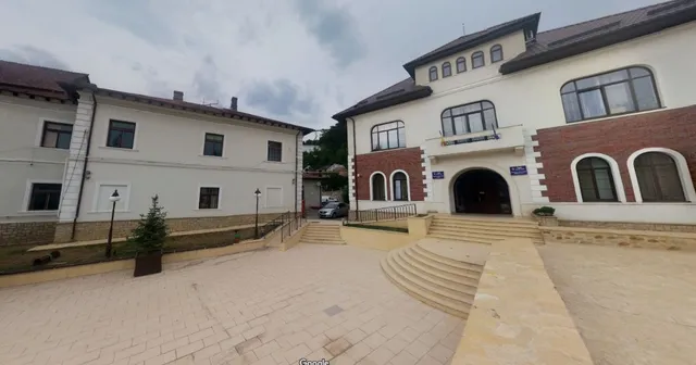 O clădire cu fațadă albă și secțiuni din cărămidă roșie prezintă ferestre negre și o intrare cu trepte curbe.