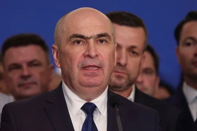 Un bărbat cu capul cal și costum bleumarin vorbește la un microfon, înconjurați de alți bărbați în fundalul albastru.