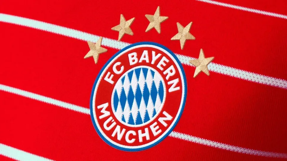 Un logo circular albastru, roșu și alb cu textul FC Bayern München este așezat pe un fundal roșu cu linii albe și cinci stele aurii.