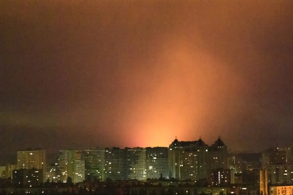 Lumina portocalie strălucește intens deasupra unei siluete de clădiri înalte sub un cer nocturn întunecat.