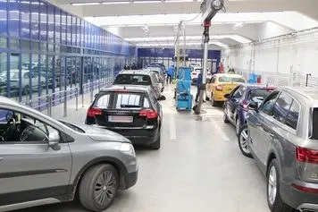 Mai multe autoturisme sunt parcate într-un atelier de service auto cu podea albă și pereți albi.