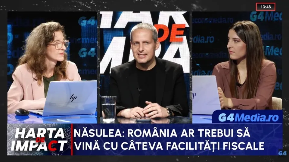 Trei persoane stau la o masă într-un studio de televiziune, având în față laptopuri, un pahar cu apă și un text informativ în partea de jos.