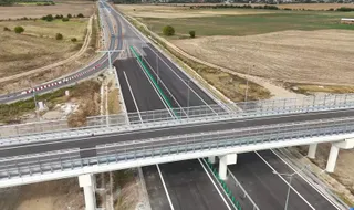 O vedere aeriană prezintă o autostradă cu mai multe benzi de asfalt, un pod peste aceasta și câmpuri deschise în fundal.