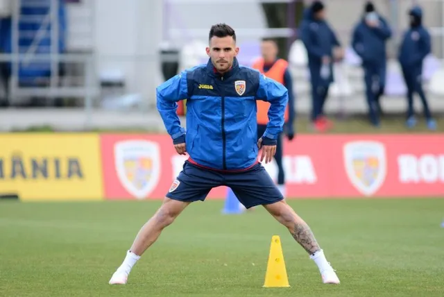 Un bărbat cu tricou și pantaloni scurți de sport albastre face exerciții de întindere pe un teren de fotbal verde.