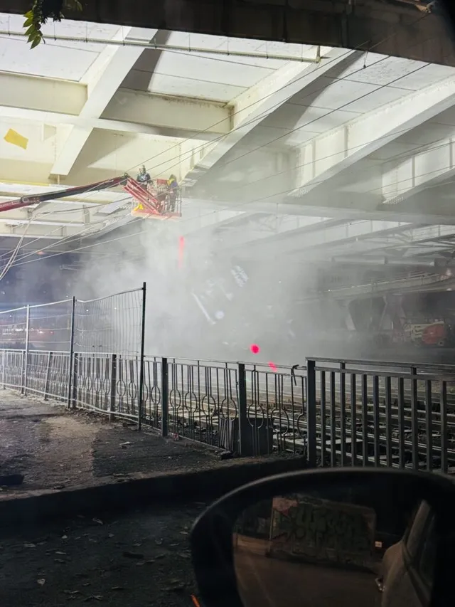 O platformă de lucru suspendată este poziționată sub o structură de beton, în timp ce un nor de fum sau praf acoperă zona de sub aceasta.
