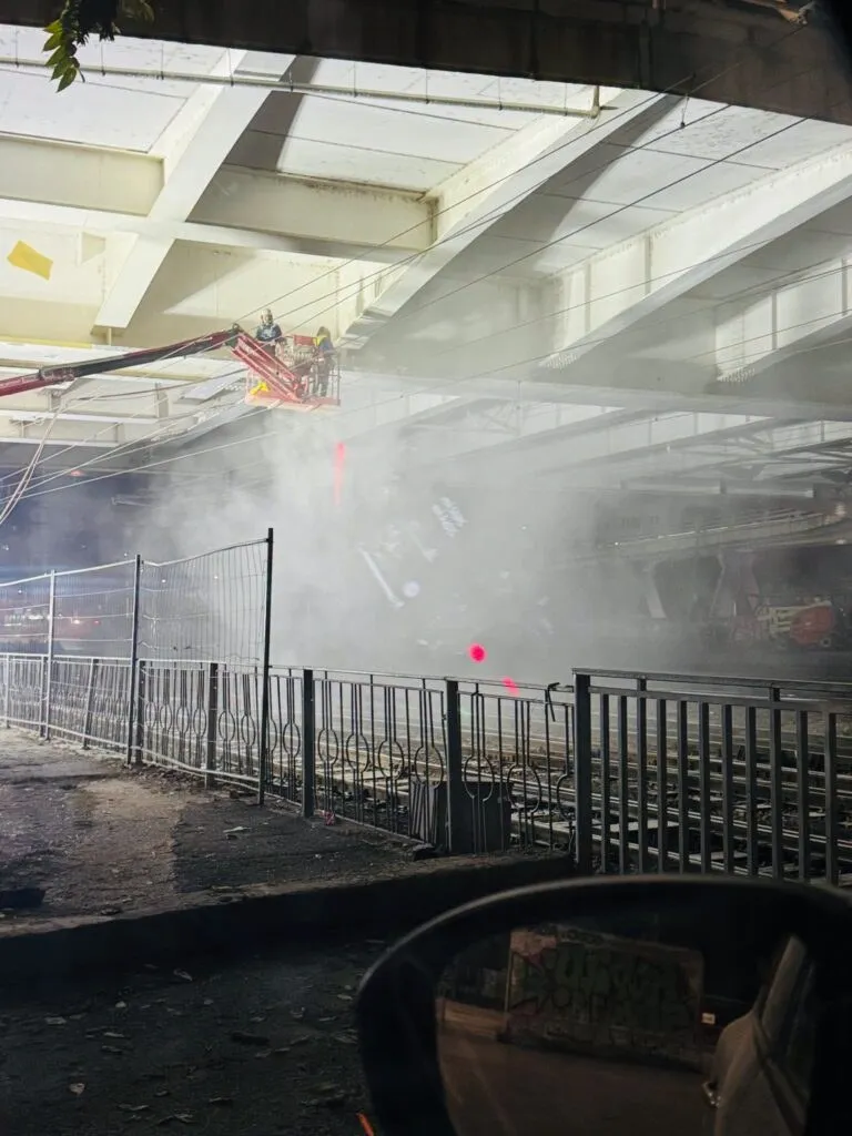 O platformă de lucru suspendată este poziționată sub o structură de beton, în timp ce un nor de fum sau praf acoperă zona de sub aceasta.