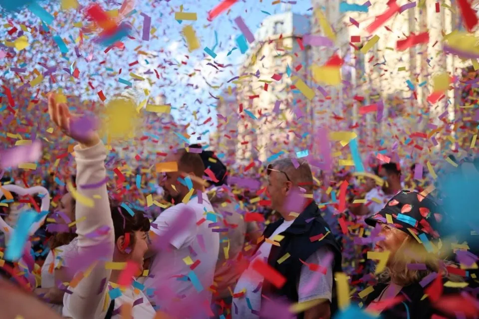 O mulțime de oameni sub un cer plin de confetti colorate, în timp ce un individ ridică brațul stâng în sus.