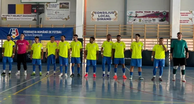 O echipă de futsal în echipamente galbene și negre stă în linie pe un teren de sport în interiorul unei săli.