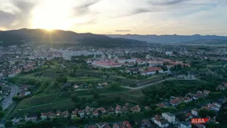 O vedere aeriană a unui oraș cu clădiri și dealuri verzi sub un cer cu soare la apus.