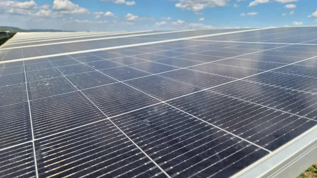 Panouri solare de culoare închisă sunt dispuse într-un rând sub un cer cu nori albi.