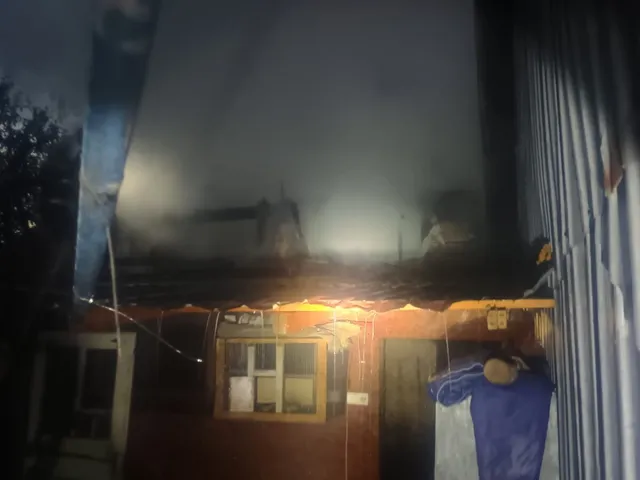 Fum dens se ridică deasupra unor structuri de depozitare în timpul nopții, lângă o clădire cu ferestre și o ușă deschisă.