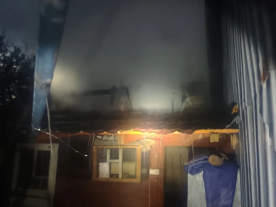 Fum dens se ridică deasupra unor structuri de depozitare în timpul nopții, lângă o clădire cu ferestre și o ușă deschisă.