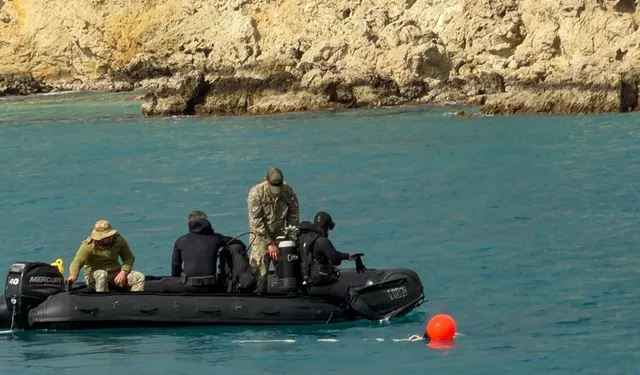 Patru persoane în echipament de culoare închisă și camuflaj se află într-o barcă cu gonflabile negru pe un lac sau o mare cu apă turcoaz.