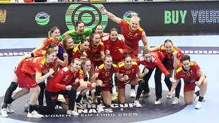 Un grup de femei îmbrăcate în echipamente sportive roșii și verzi pozează împreună pe un teren de sport de culoare albastră.