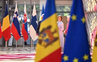Două femei stau în picioare într-o încăpere cu mai multe steaguri colorate dispuse în rânduri.