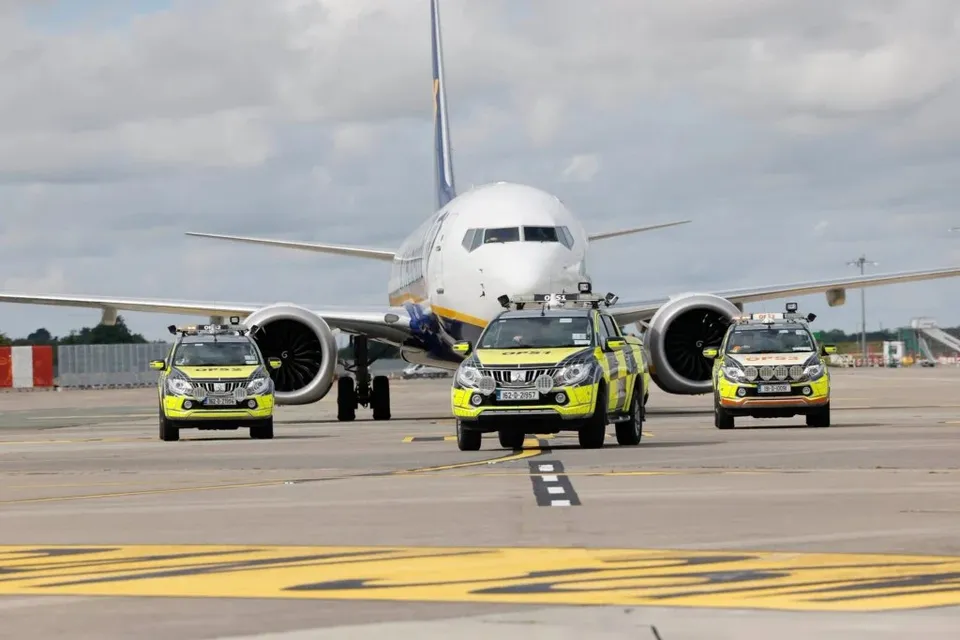 Un avion de pasageri alb stă pe o pistă de aeroport în spatele a trei mașini de poliție de culoare galbenă și gri.