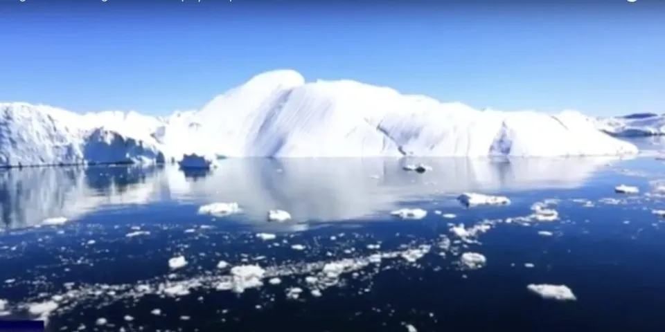 O masă mare de gheață albă plutește pe un lac sau ocean albastru sub un cer senin.
