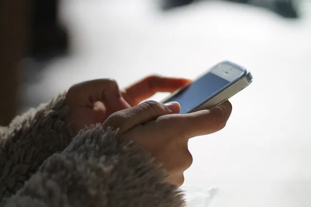 O persoană ține un telefon mobil cu ambele mâini și folosește degetul pentru a interacționa cu ecranul dispozitivului.