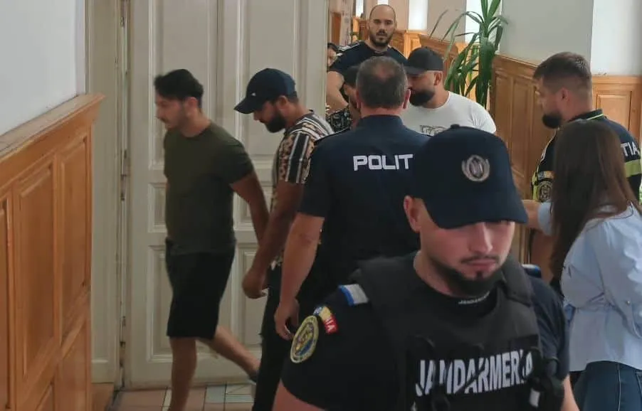 Un grup de bărbați merge pe un hol lângă un ofițer de poliție și un jandarm în uniformă neagră.