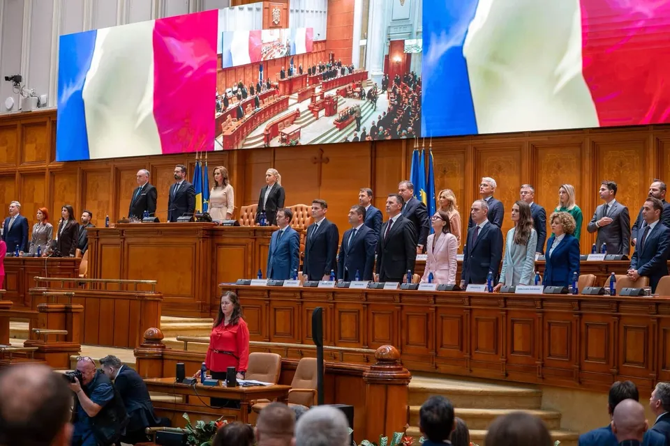 Oamenii stau în rând în fața unui pupitru de lemn într-o sală de conferințe cu draperi mari colorate pe perete.