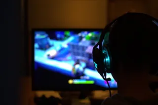 O persoană cu căști de pe cap privește un monitor care afișează imagini colorate într-o cameră întunecată.