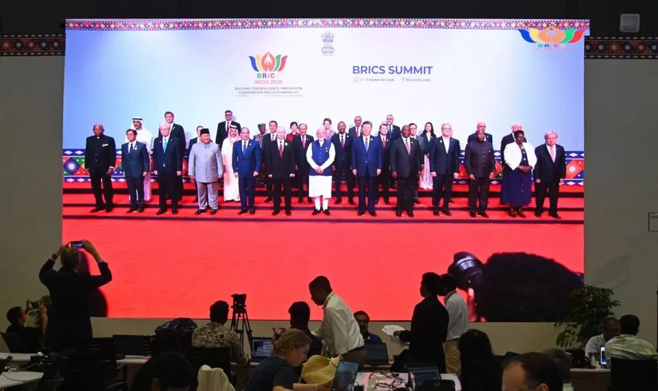 Un grup de lideri în costume oficiale stă în rând pe un podium roșu în fața unui ecran mare cu textul BRICS SUMMIT.