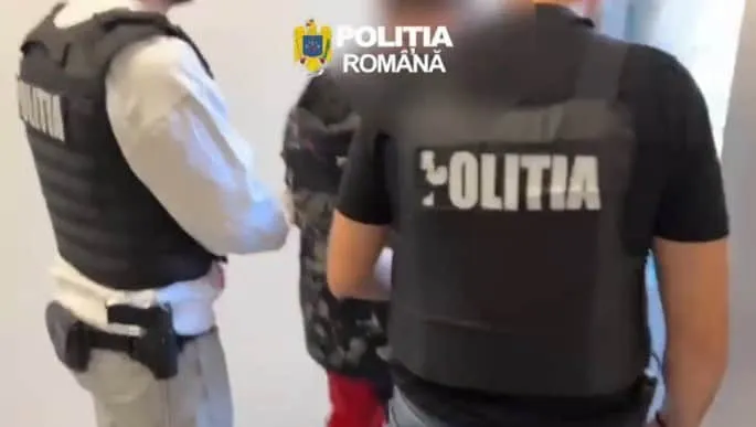 Unii polițiști în uniformă neagră cu inscripcția POLITIA sunt văzuți din spate, purtând veste tactice și echipament de serviciu.