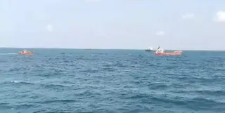 Trei nave mici navighează pe o suprafață de apă de culoare albastru-închis sub un cer deschis și luminos.