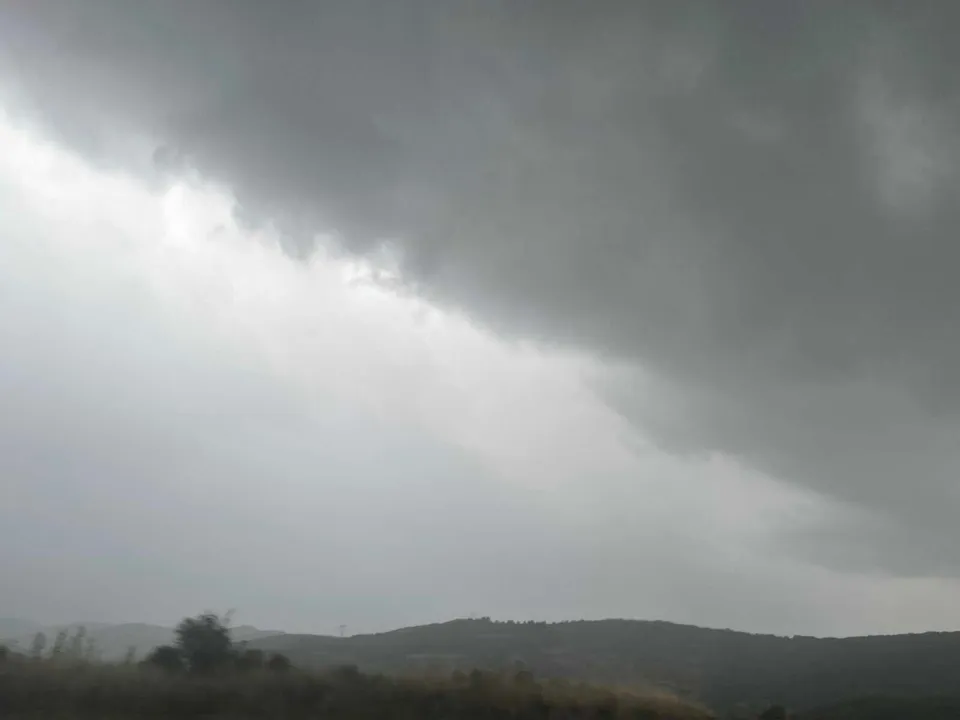 Cerul este acoperit de nori gri deasupra unor dealuri întunecate sub un strop de lumină albă.