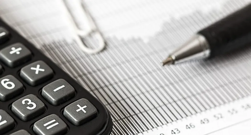 Un calculator de buzunar negru, un pix și un document cu grafice de tip bare sunt așezate pe o suprafață plană.